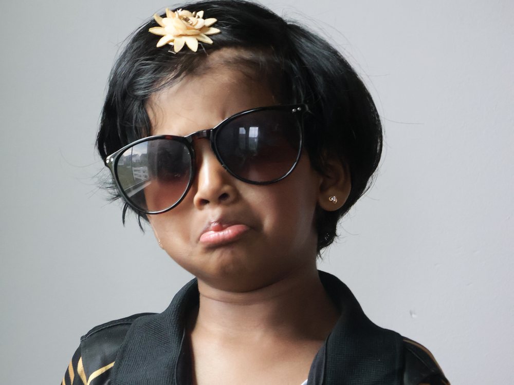 Portrait of a young girl in sunglasses and a team jersey against a plain grey backdrop